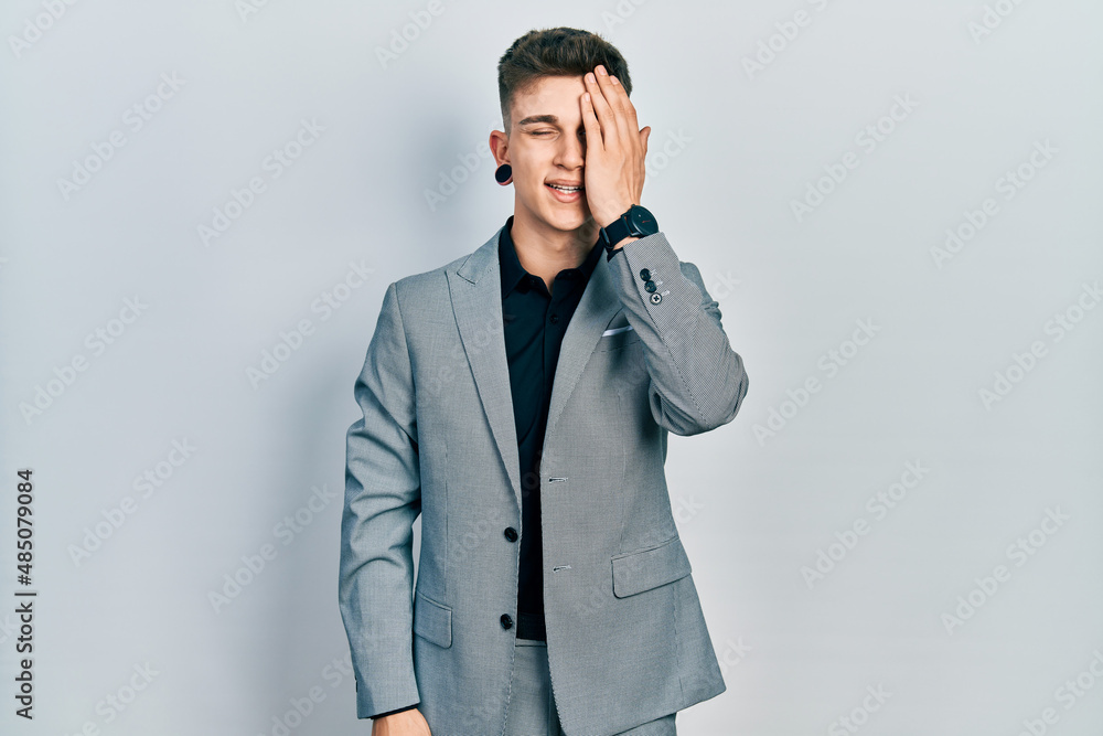 Young caucasian boy with ears dilation wearing business jacket covering one eye with hand, confident smile on face and surprise emotion. Young caucasian boy with ears dilation wearing business jacket covering one eye with hand, confident smile on face and surprise emotion.