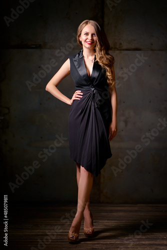 Studio Portrait of Beautiful young woman with long hair in little black dress against dark background.