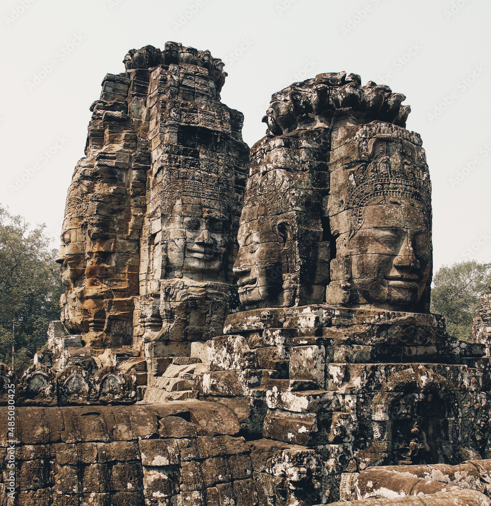 Sculpture of a head -  serenely smiling faces -  on the ruins of an ancient stone temple lost in the Cambodian jungle - Bayon of Angkor temples