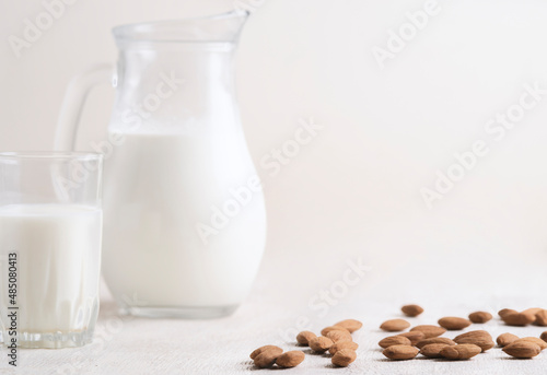 Alternative milk of almonds in a glass and glass jug on a wooden background. copy space