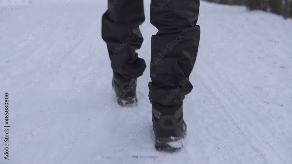 Shot showing man grey hiking boots while he walks outdoors at slow pace on the snow and ice in the middle of the mountains. Rear view, slowly focus subject at the beginning Shot showing man grey hiking boots while he walks outdoors at slow pace on the snow and ice in the middle of the mountains. Rear view, slowly focus subject at the beginning