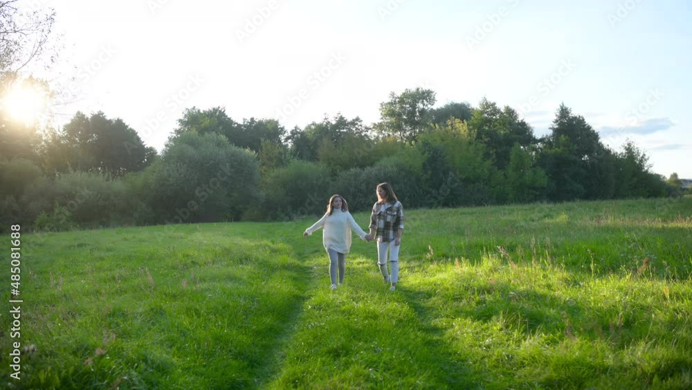 Happy young mum and daughter walking together outdoor enjoy beautiful field of sunshine and spring grass while on a summer holiday. Family outdoor lifestyle. Happy young mum and daughter walking together outdoor enjoy beautiful field of sunshine and spring grass while on a summer holiday. Family outdoor lifestyle.