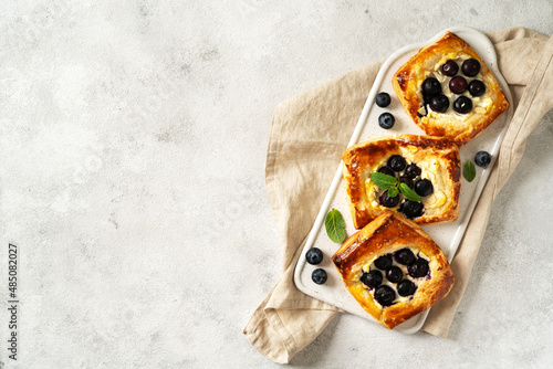 Mini puff pie with cheese cream, almonds, and blueberries in a plate on the kitchen table. Delicious layered square with berries, dorblue or ricotta, nuts on a culinary background. Top view
