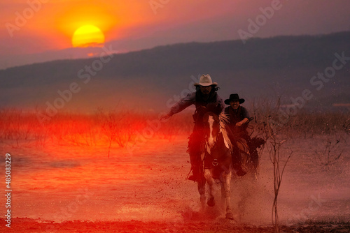 Silhouette of a cowboy riding a horse wading through the water at sunset behind a mountain.