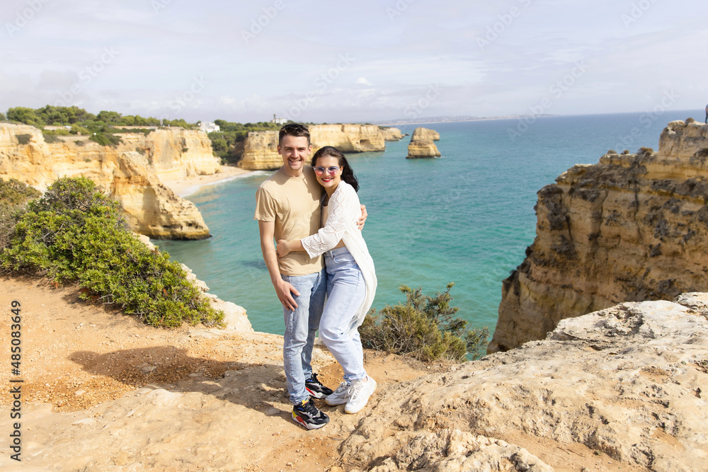 young beautiful couple stands on a rock against the backdrop of the beach and ocean beach in Portugal