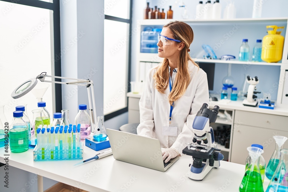 Young blonde woman wearing scientist uniform using laptop at laboratory