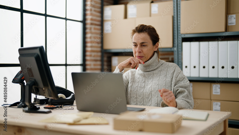 Middle age hispanic woman ecommerce business worker using laptop at storehouse office Middle age hispanic woman ecommerce business worker using laptop at storehouse office