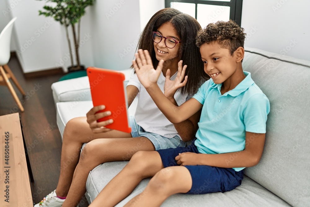 Brother and sister having video call using touchpad sitting on sofa at home Brother and sister having video call using touchpad sitting on sofa at home
