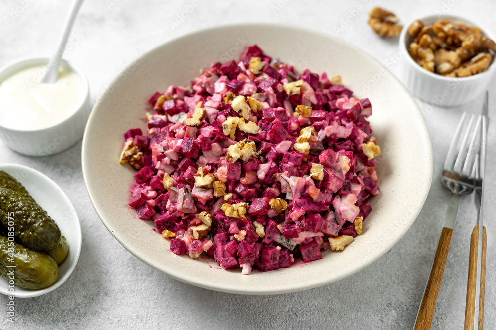 Beetroot salad with pickled cucumbers, walnuts, apple and mayonnaise in a bowl on a light gray kitchen table closeup Beetroot salad with pickled cucumbers, walnuts, apple and mayonnaise in a bowl on a light gray kitchen table closeup