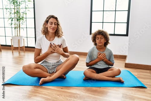 Young woman and son sitting on training mat at the gym smiling with hands on chest with closed eyes and grateful gesture on face. health concept.