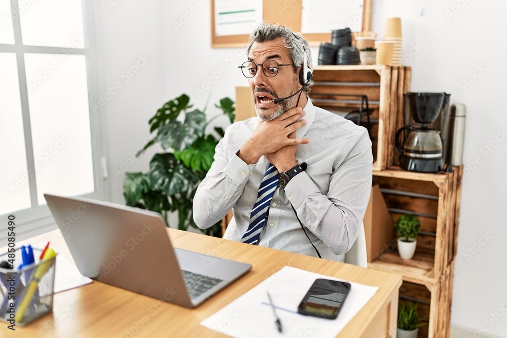 Middle age hispanic business man working at the office wearing operator headset shouting and suffocate because painful strangle. health problem. asphyxiate and suicide concept. Middle age hispanic business man working at the office wearing operator headset shouting and suffocate because painful strangle. health problem. asphyxiate and suicide concept.
