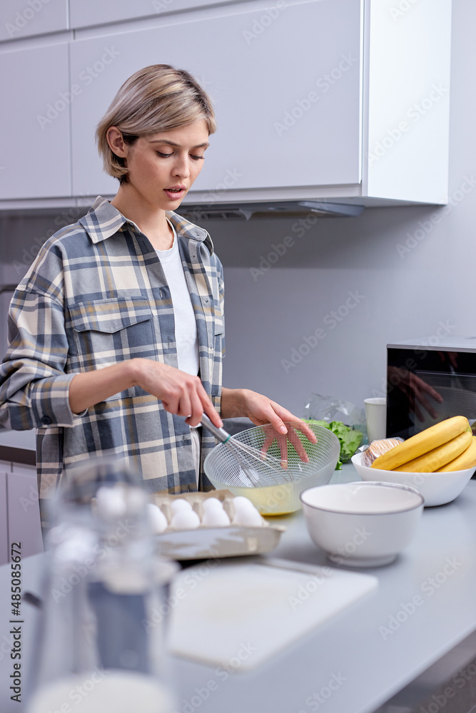 Woman in kitchen during cooking biscuits, mixing dough in bowl, holidays at home. Attractive short haired female in casual shirt enjoying baking cooking, pretty housewife engaged in cooking