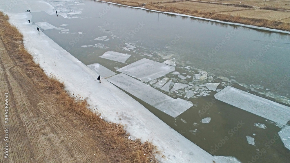Workers use long poles to push ice on the water, North China
