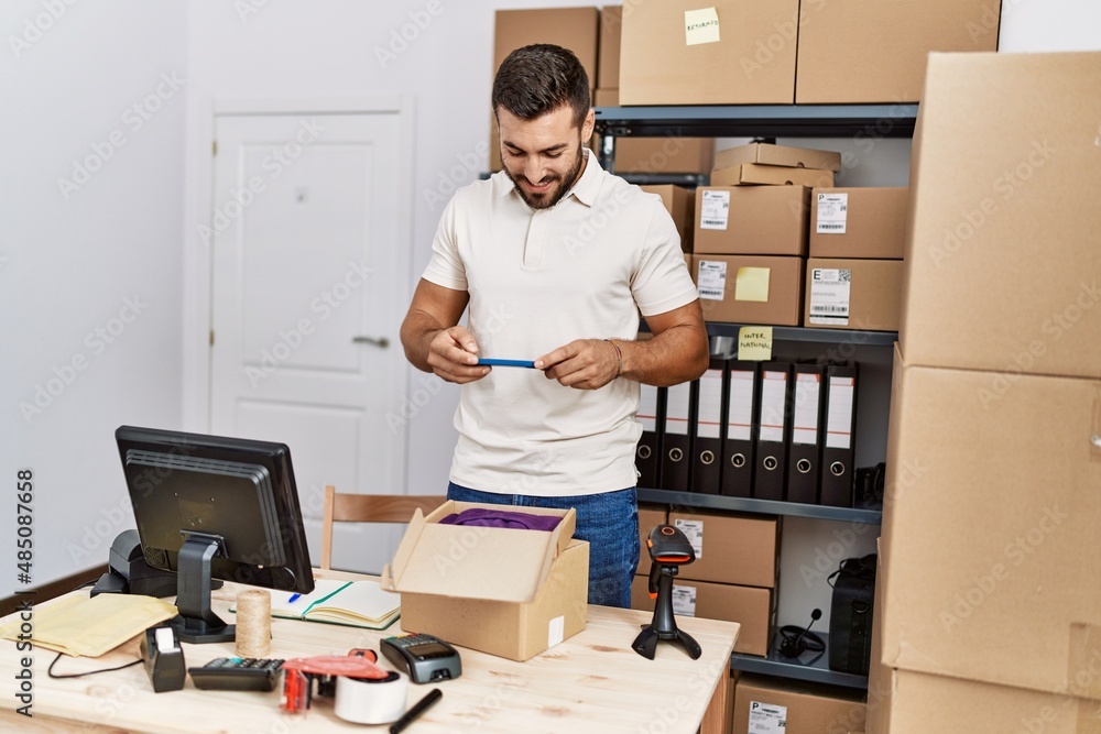 Young hispanic man smiling confident make photo to t shirt package at storehouse Young hispanic man smiling confident make photo to t shirt package at storehouse