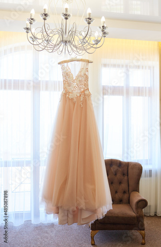 Luxury wedding dress hanging on the chandelier in a hotel room. Bridal gown. Wedding