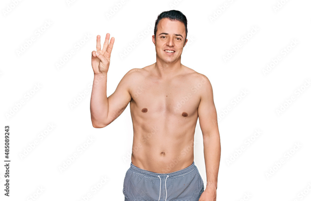 Handsome young man wearing swimwear shirtless showing and pointing up with fingers number three while smiling confident and happy. Handsome young man wearing swimwear shirtless showing and pointing up with fingers number three while smiling confident and happy.