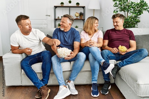Group of middle age caucasian friends smiling happy watching movie at home.