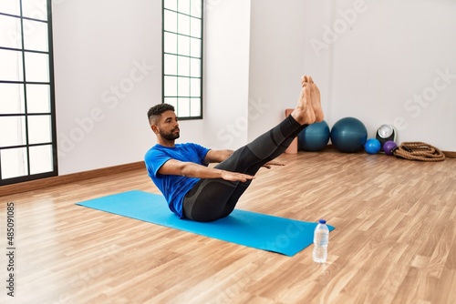 Handsome hispanic man doing exercise and stretching on yoga mat, practicing flexibility and training at the gym