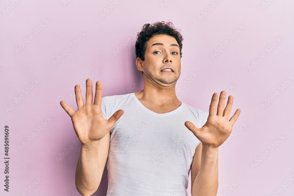 Young handsome man wearing casual white t shirt afraid and terrified with fear expression stop gesture with hands, shouting in shock. panic concept. Young handsome man wearing casual white t shirt afraid and terrified with fear expression stop gesture with hands, shouting in shock. panic concept.