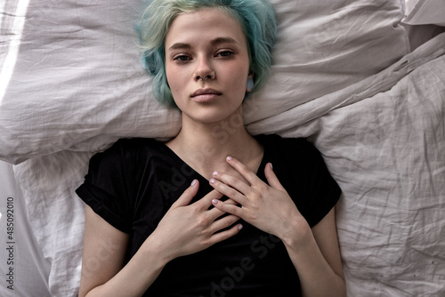 Unhappy exhausted woman lying on bed, suffering from headache or migraine, feeling unwell, suffering from insomnia, lack of sleep, top view on young caucasian female depressed, feel bad