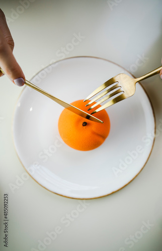 orange cake in the form of an orange or tangerine top view. cake on a white plate with golden cutlery.