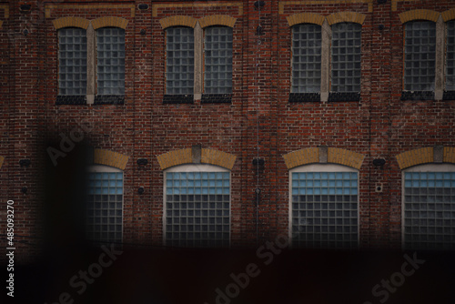 photographed part of an old brick factory without plaster. The windows are made of thick glass cubes, built on top of each other. At the bottom of the photo is a part of the fence.