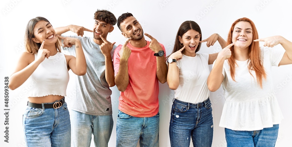 Obraz premium Group of young friends standing together over isolated background smiling cheerful showing and pointing with fingers teeth and mouth. dental health concept.