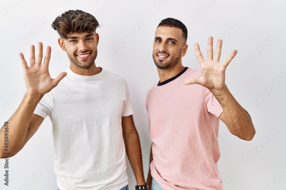 Young gay couple standing over isolated background showing and pointing up with fingers number ten while smiling confident and happy. Young gay couple standing over isolated background showing and pointing up with fingers number ten while smiling confident and happy.