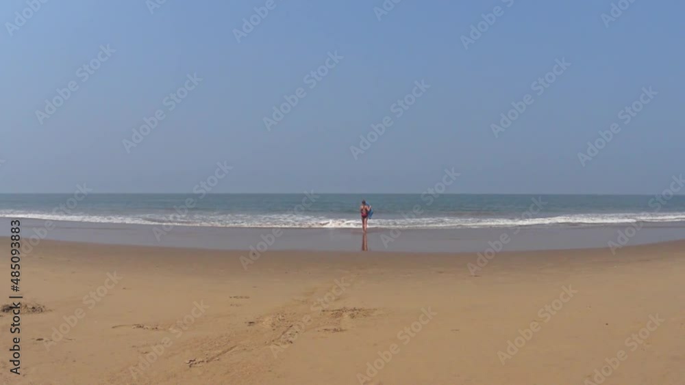a girl in a swimsuit walks into the sea with a swimming board, India