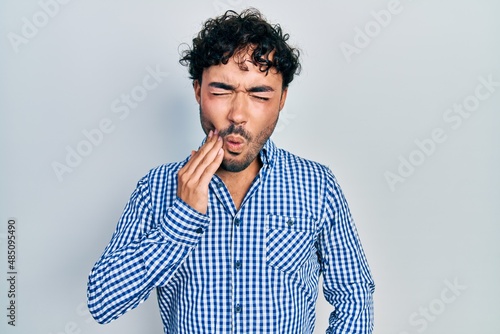 Young hispanic man wearing casual clothes touching mouth with hand with painful expression because of toothache or dental illness on teeth. dentist