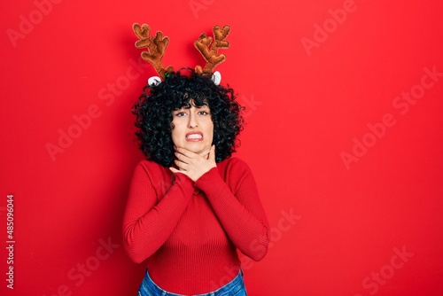 Young middle east woman wearing cute christmas reindeer horns shouting and suffocate because painful strangle. health problem. asphyxiate and suicide concept.