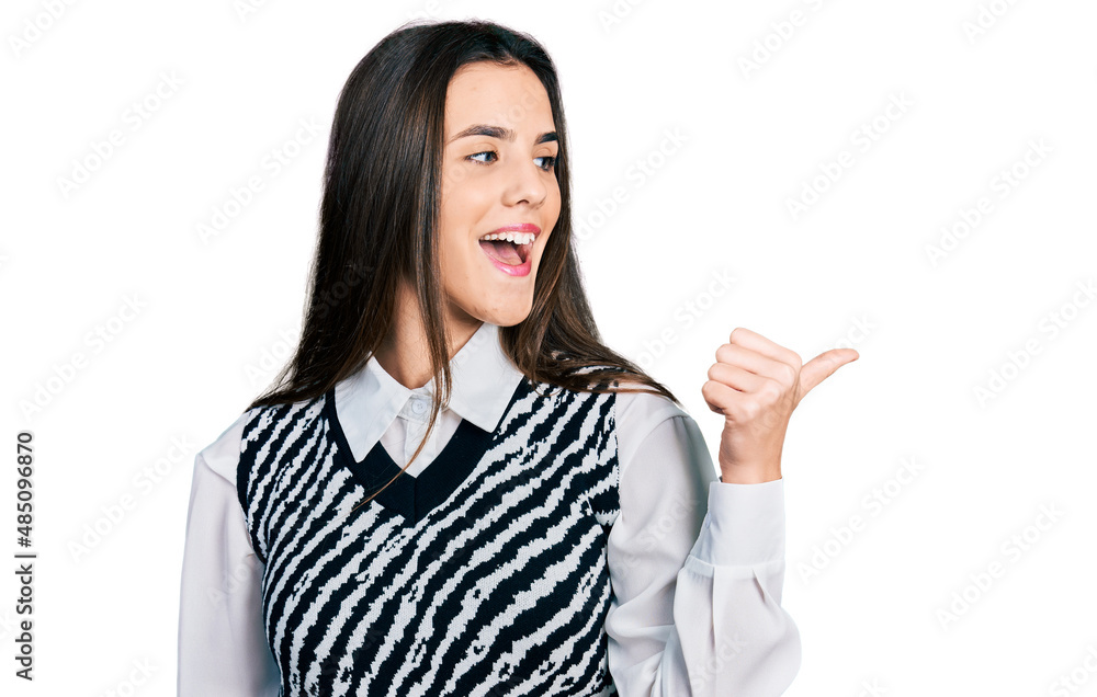 Young brunette teenager wearing casual elegant look pointing thumb up to the side smiling happy with open mouth Young brunette teenager wearing casual elegant look pointing thumb up to the side smiling happy with open mouth