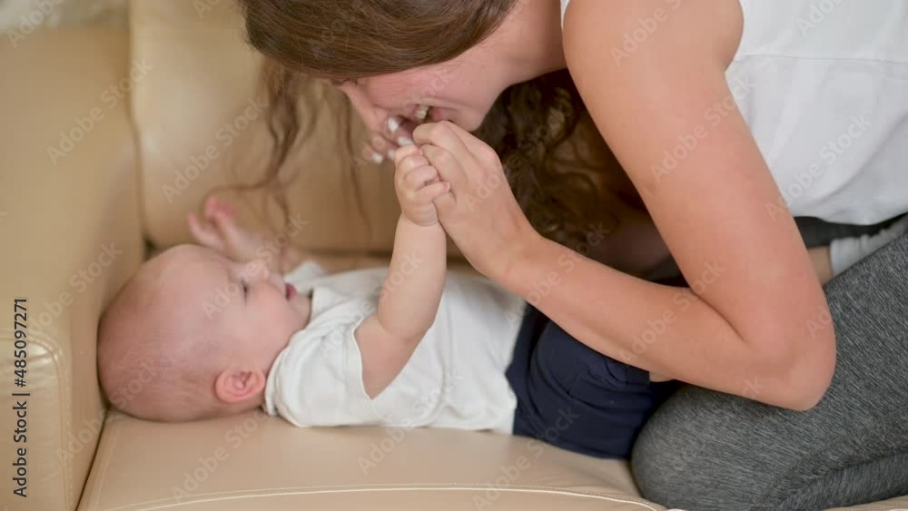 Young happy mother is playing with her newborn baby on the sofa in the morning. smiling mum enjoying bonding cuddling hugging spending time with baby. Parenthood, Childhood. Young happy mother is playing with her newborn baby on the sofa in the morning. smiling mum enjoying bonding cuddling hugging spending time with baby. Parenthood, Childhood.