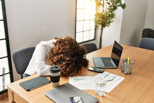 Middle age hispanic woman overworked with head on table at office photo