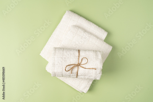 Flat lay, a stack of clean, fresh white towels on a light green background.