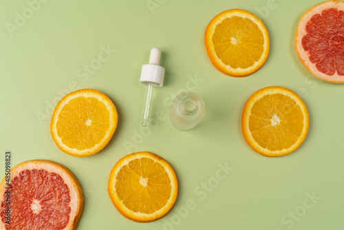 Natural vitamin C serum, skin care, essential oils. Cosmetic glass bottle with dropper and fresh juicy orange and grapefruit slices.
