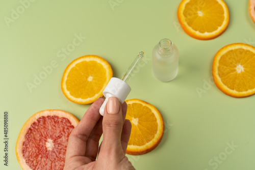 Natural vitamin C serum, skin care, essential oils. Cosmetic glass bottle fresh juicy slices of oranges and grapefruits. A woman's hand holds a pipette. photo