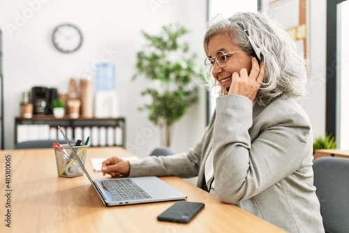 Middle age grey-haired call center agent woman smiling happy working at the office.
