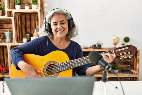 Middle age grey-haired woman playing guitar working at radio studio.