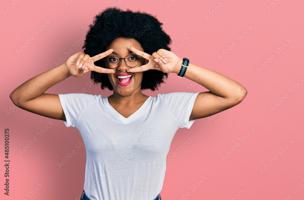Young african american woman wearing casual white t shirt doing peace symbol with fingers over face, smiling cheerful showing victory Young african american woman wearing casual white t shirt doing peace symbol with fingers over face, smiling cheerful showing victory
