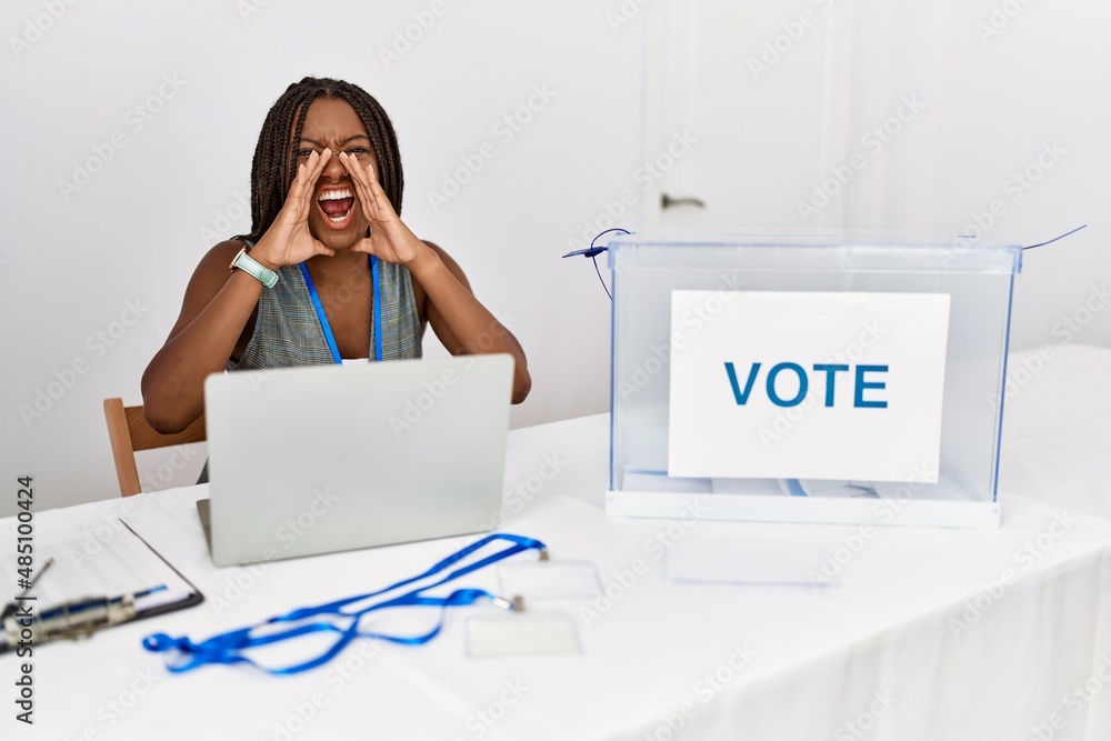 Young african american woman working at political election sitting by ballot shouting angry out loud with hands over mouth Young african american woman working at political election sitting by ballot shouting angry out loud with hands over mouth