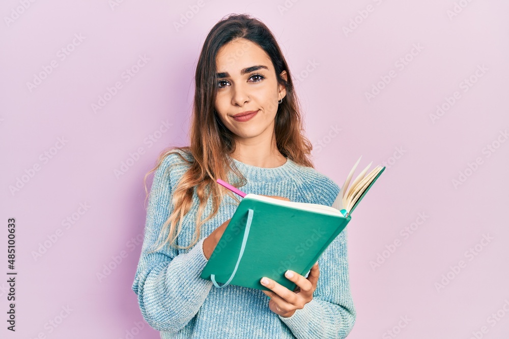 Young hispanic girl reading and writing book relaxed with serious expression on face. simple and natural looking at the camera. Young hispanic girl reading and writing book relaxed with serious expression on face. simple and natural looking at the camera.
