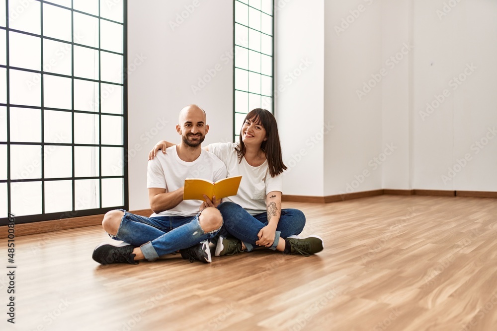 Young hispanic couple smiling happy reading book at empty new home. Young hispanic couple smiling happy reading book at empty new home.