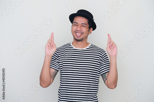Tattooed Asian man doing finger crossed sign with happy face expression photo