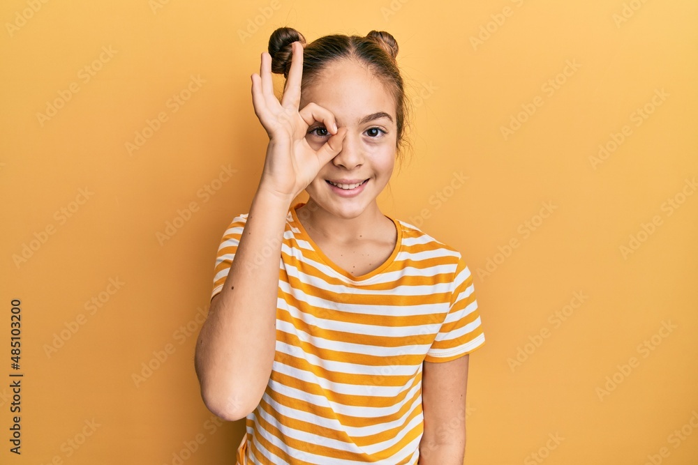 Beautiful brunette little girl wearing casual striped t shirt doing ok gesture with hand smiling, eye looking through fingers with happy face. Beautiful brunette little girl wearing casual striped t shirt doing ok gesture with hand smiling, eye looking through fingers with happy face.