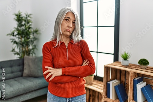 Middle age grey-haired woman wearing casual clothes standing at home skeptic and nervous, disapproving expression on face with crossed arms. negative person.