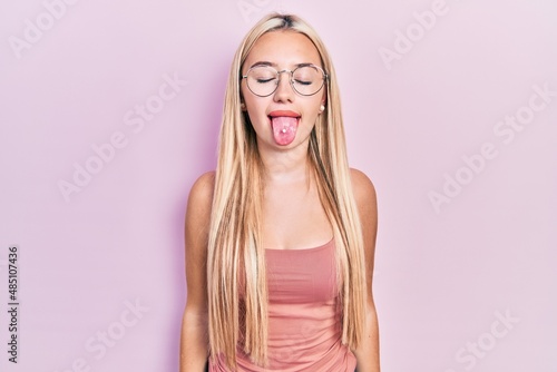 Young blonde girl wearing casual clothes sticking tongue out happy with funny expression. emotion concept.