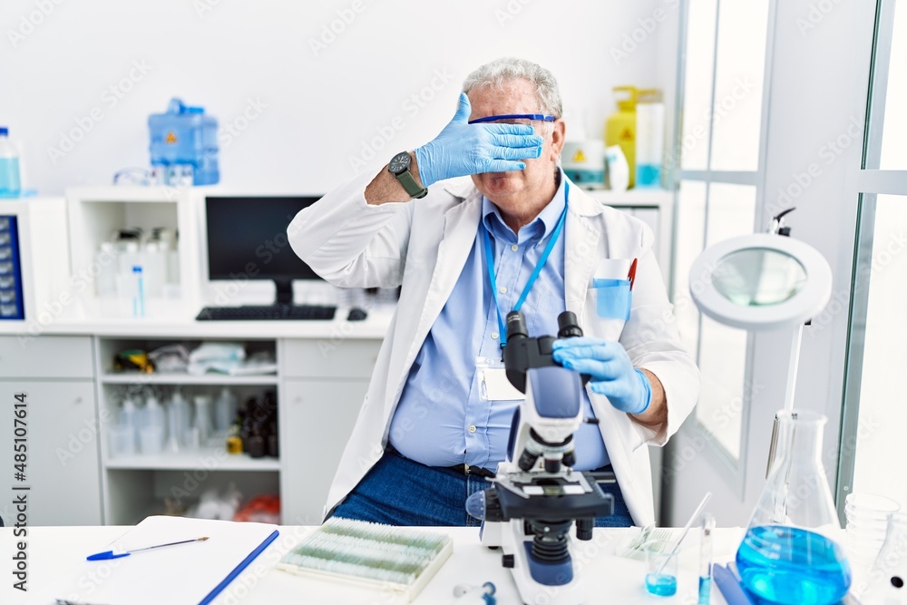 Senior caucasian man working at scientist laboratory covering eyes with hand, looking serious and sad. sightless, hiding and rejection concept Senior caucasian man working at scientist laboratory covering eyes with hand, looking serious and sad. sightless, hiding and rejection concept