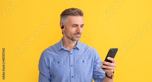 smiling man using phone in headphones on yellow background, communication © Olena