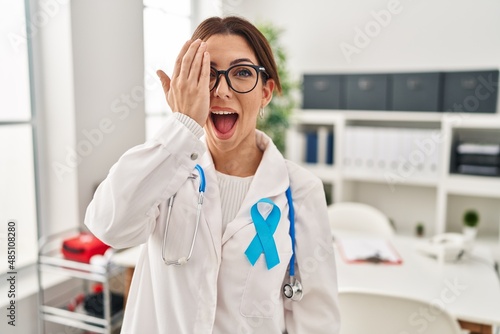 Young brunette doctor woman wearing stethoscope at the clinic covering one eye with hand  confident smile on face and surprise emotion.